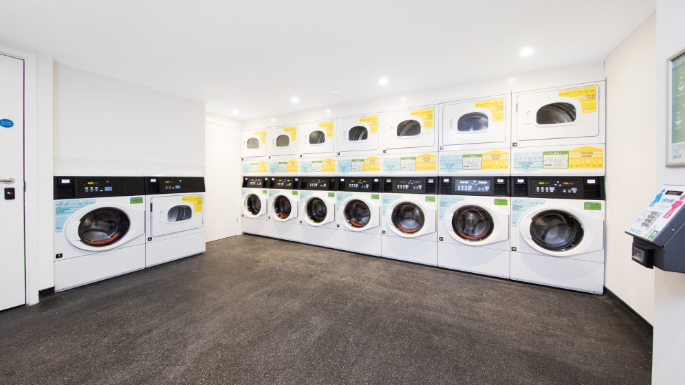 A laundry with a row of seven washing machines and dryers stacked on top